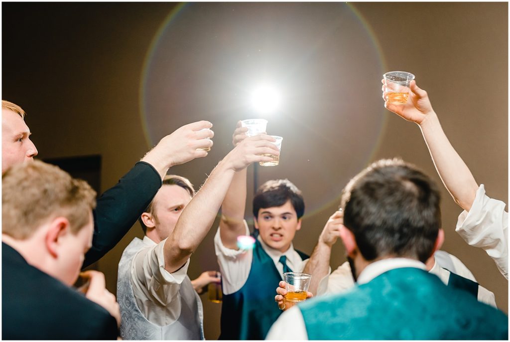 groomsmen holding up drinks during wedding reception