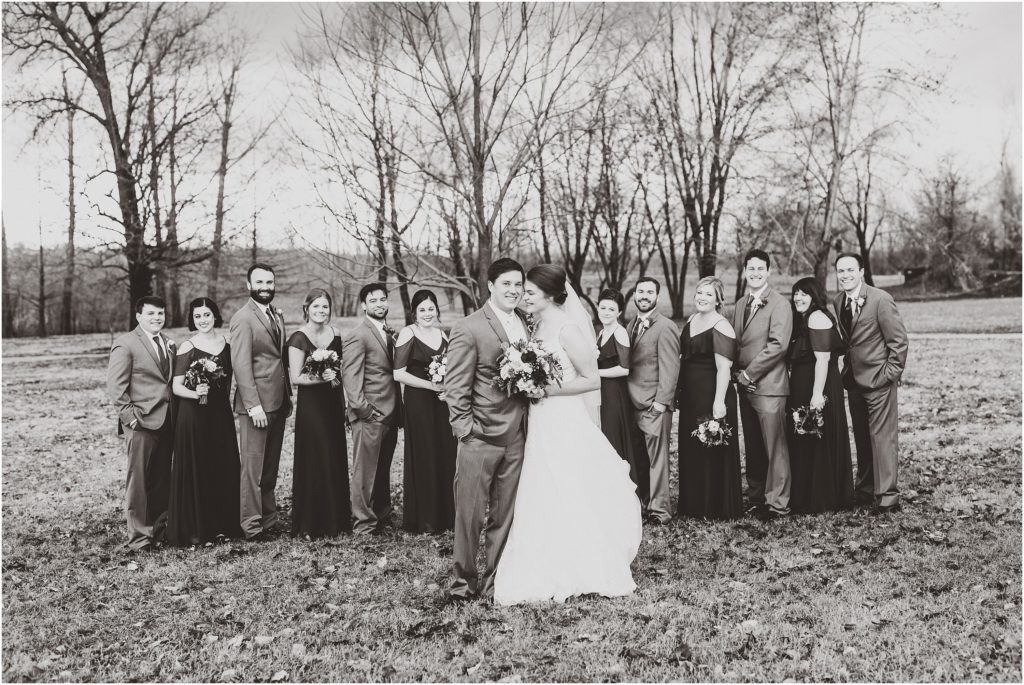 black and white photo of wedding party smiling behind bride and groom