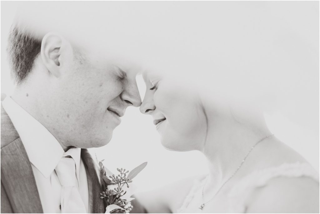 black and white photo of bride and groom nuzzling under veil