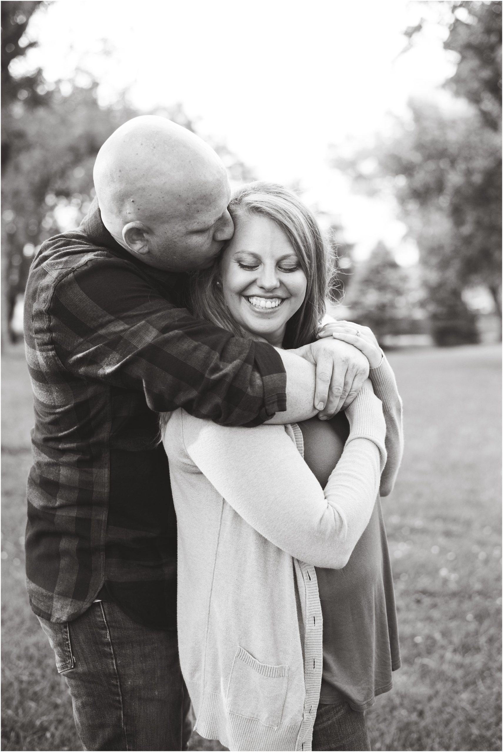 black and white image of man holding fiancé and girl smiling down at shoulder for engagement session in Jefferson City, mo