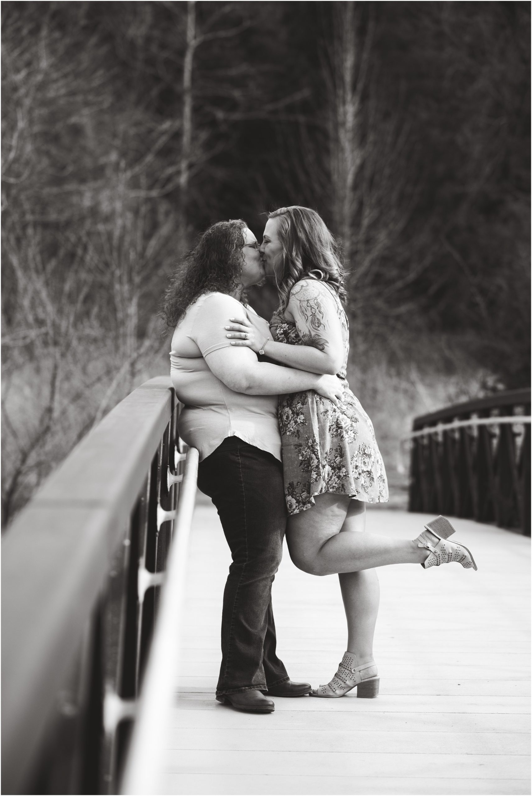 black and white image of engaged lesbian couple kissing on bridge in park