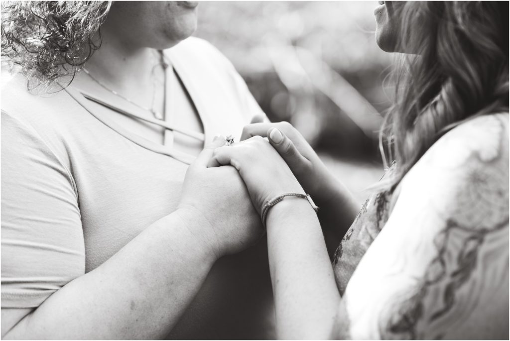 black and white image of lesbian couple holding hands and details of engagement rings