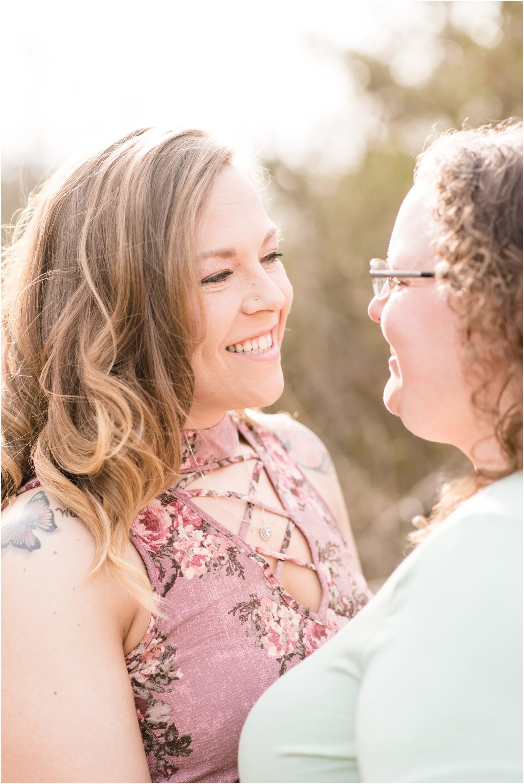 engaged couple smiling at each other during engagement session wearing pink and blue