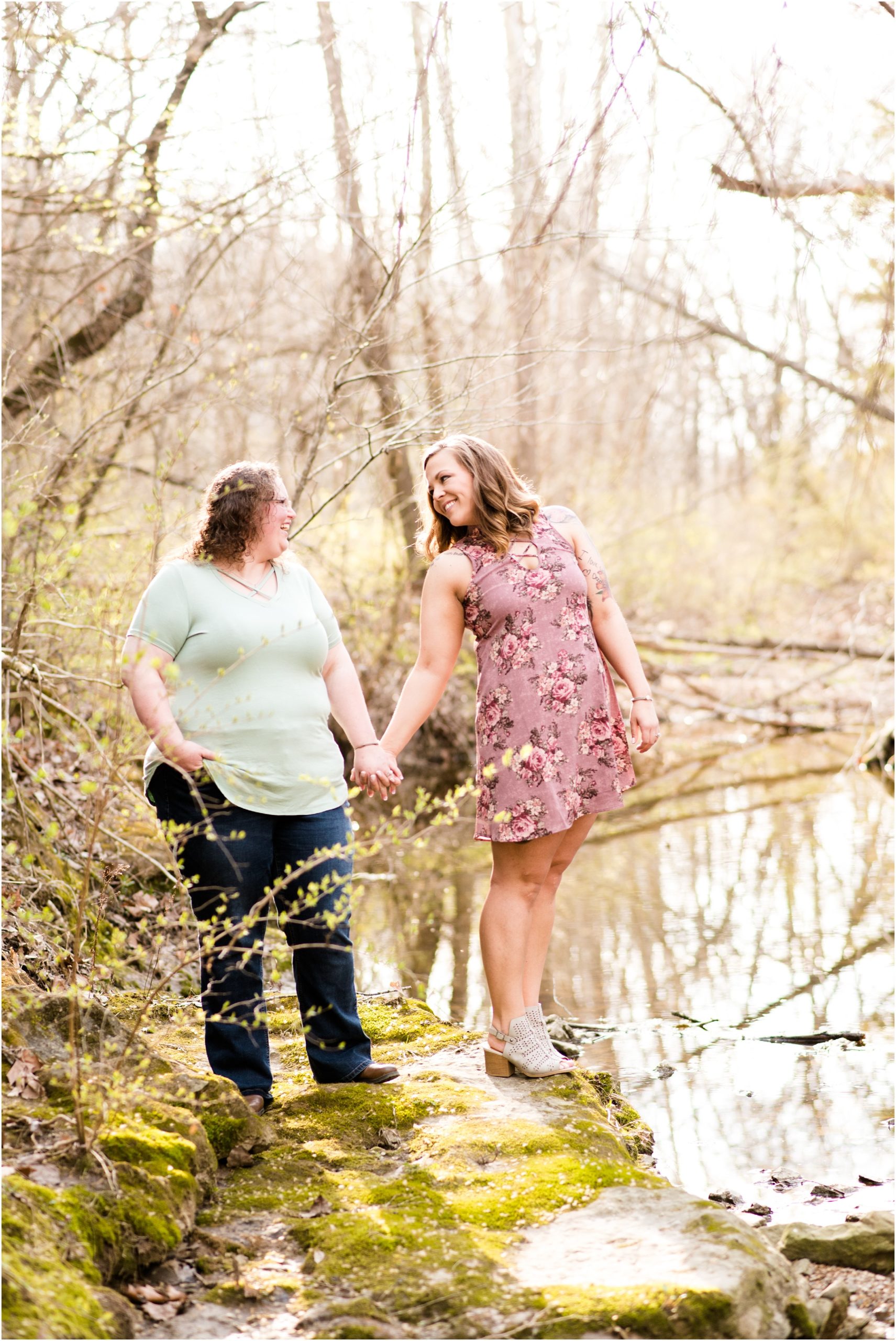 engaged female couple standing on rocks by creek at Jefferson City greenway trail engagement session
