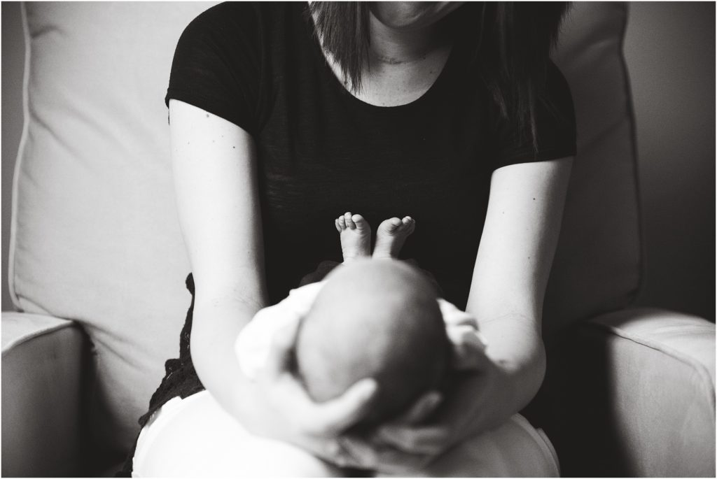 black and white image of newborn laying on mom's lap with focus on feet