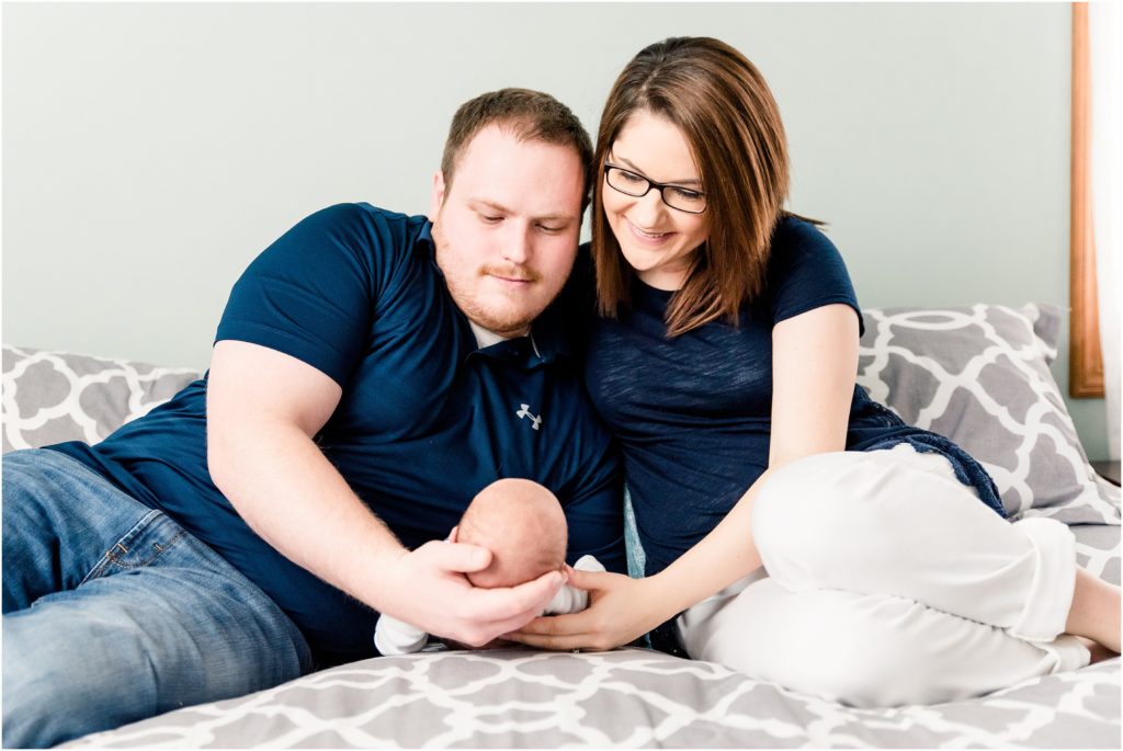 mom and dad holding newborn boy on bed smiling at him