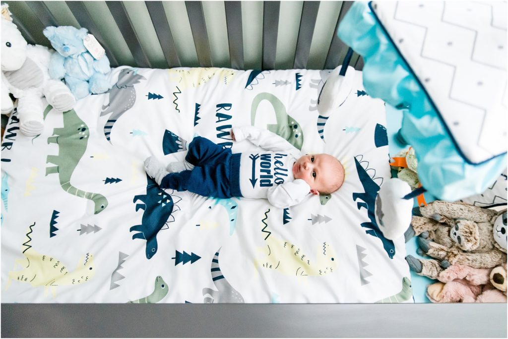 newborn boy in dinosaur themed nursery laying in crib with hello world onesie on