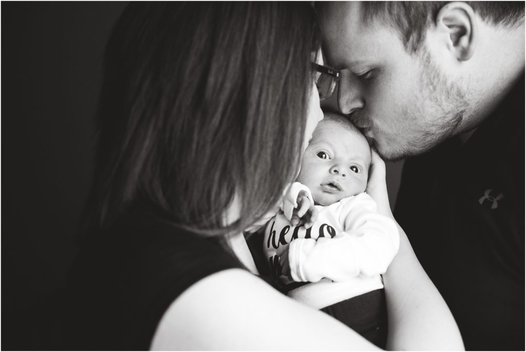 black and white image of mom and dad kissing baby boy on head