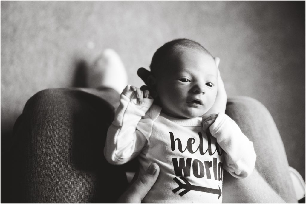 black and white image of baby boy in hello world onesie laying on dad's lap staring up at dad for jefferson city newborn session