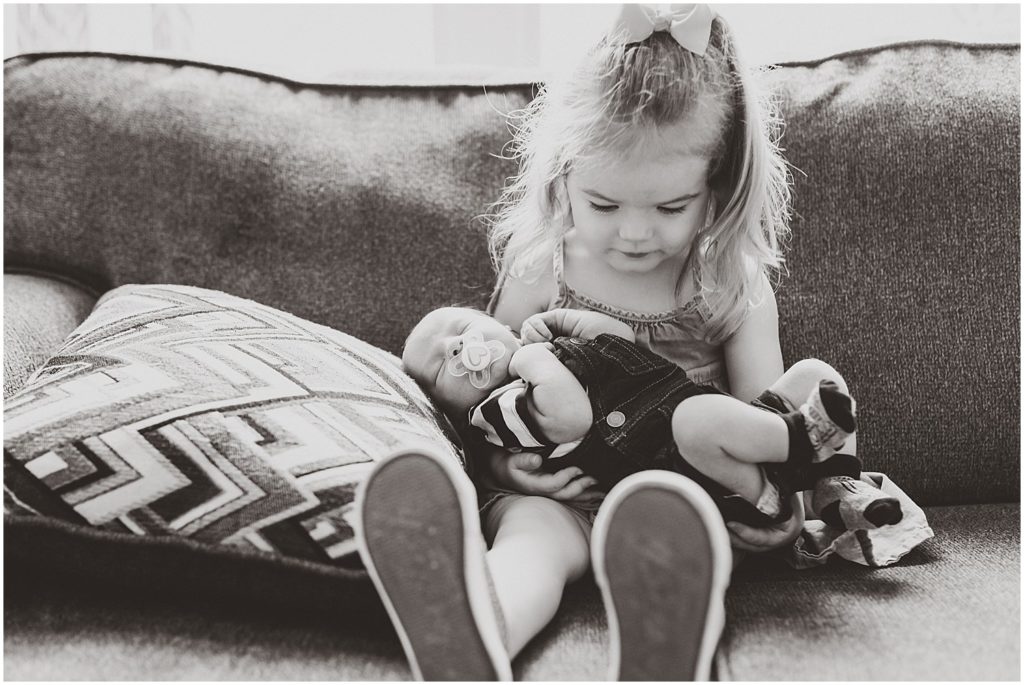 black and white image of big sister holding baby brother on couch