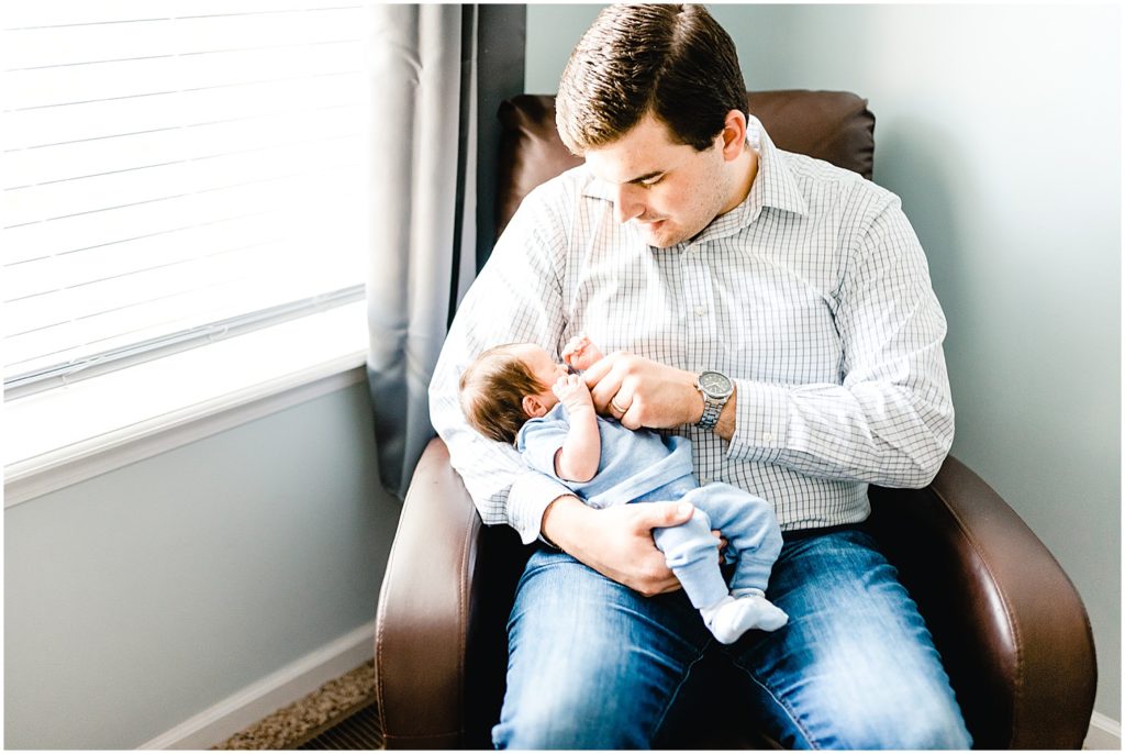 dad holding baby boy in chair next to window for newborn session