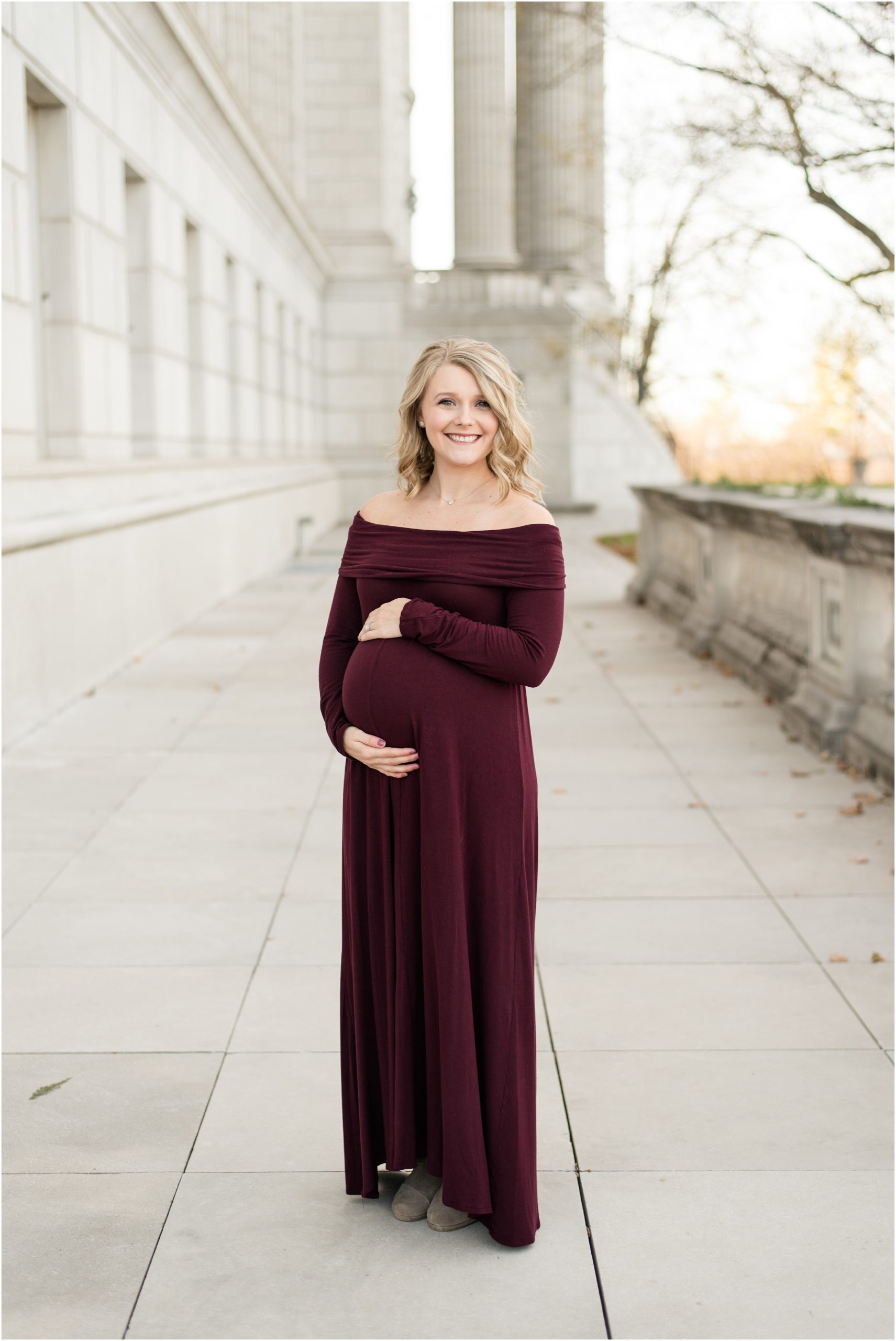expecting mother holding belly and smiling at camera for missouri state capitol maternity session