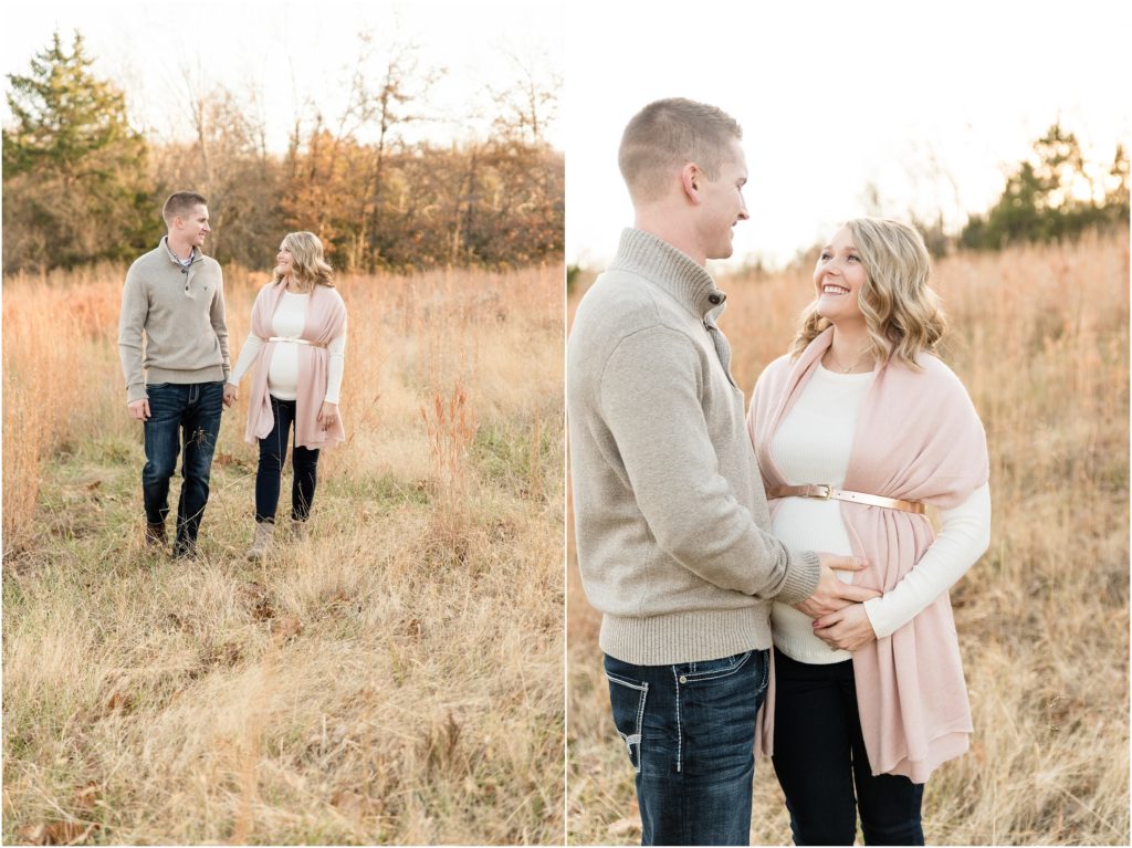 couple smiling at each other holding baby belly in field for maternity session