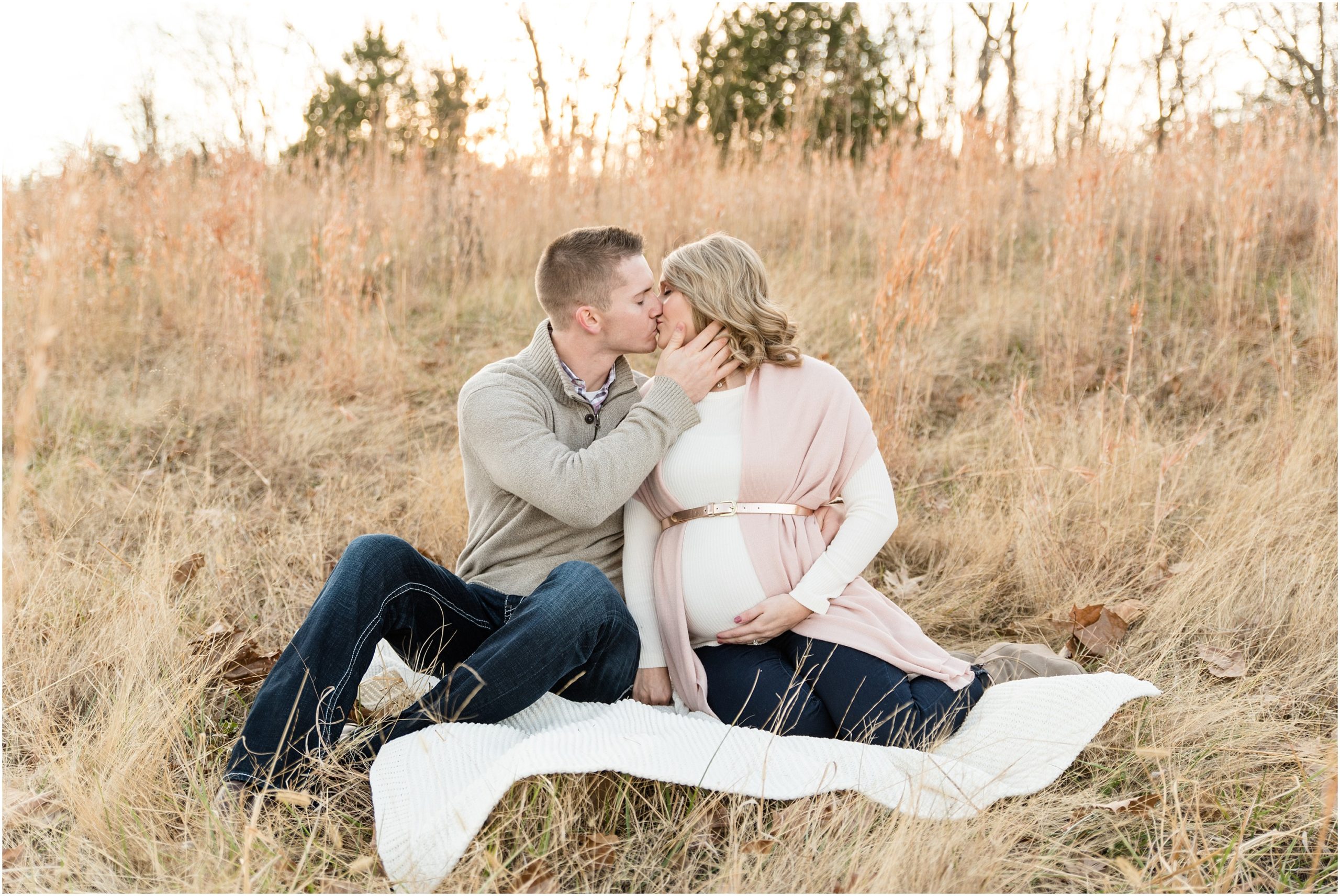 couple sitting in tall grasses holding belly and kissing for maternity session at binder park