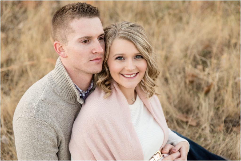couple sitting down smiling at camera and holding baby belly for maternity session