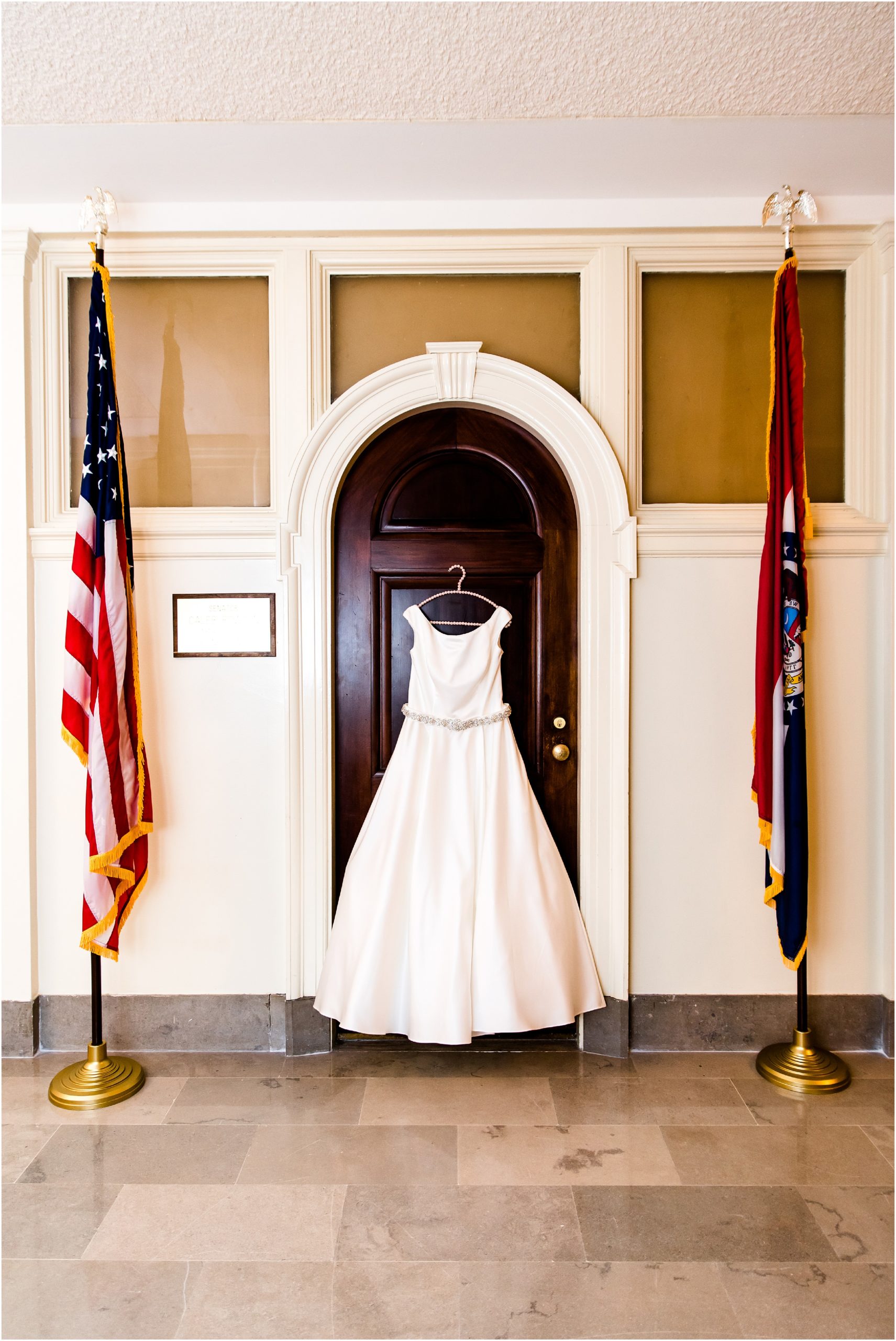 wedding dress hanging on office door for missouri state capitol wedding with US flag and Missouri flag on either side