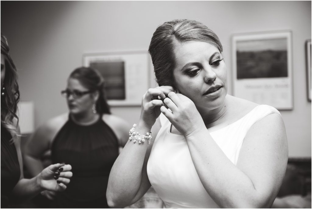 black and white image of bride putting earrings on in getting ready room before wedding