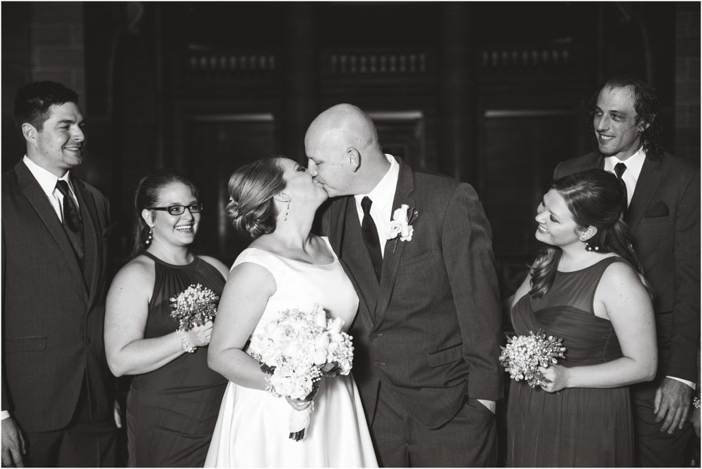 black and white image of bride and groom kissing with bridal party