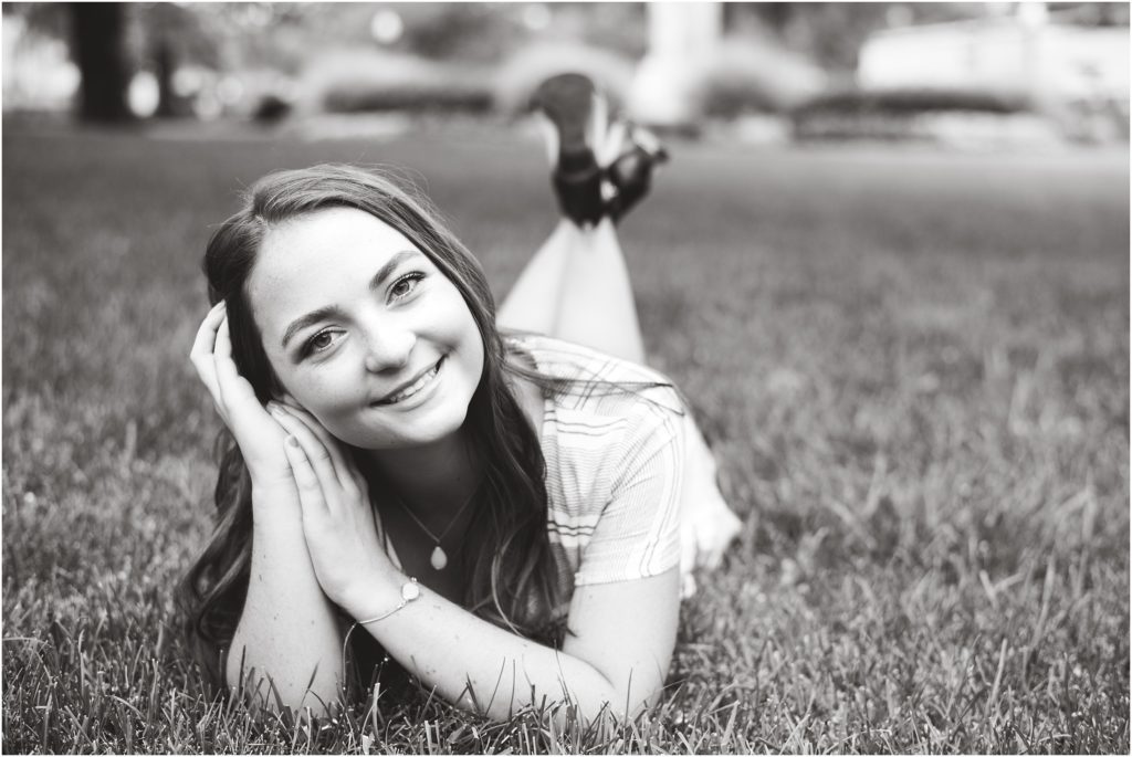 black and white image of senior girl laying in the grass smiling for senior photos
