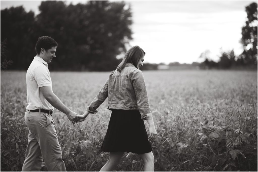 black and white image of couple walking together in field by Katy Trail for engagement session