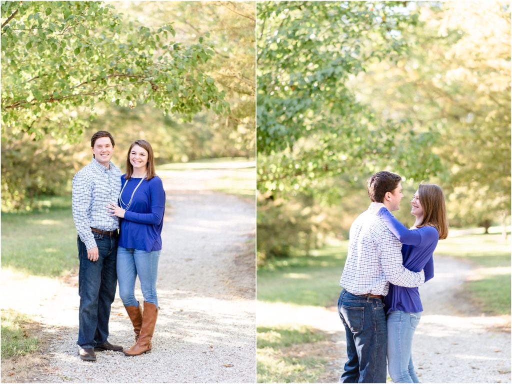 engaged couple standing on gravel path in tree covered area of park with sunlight wearing blue shirts