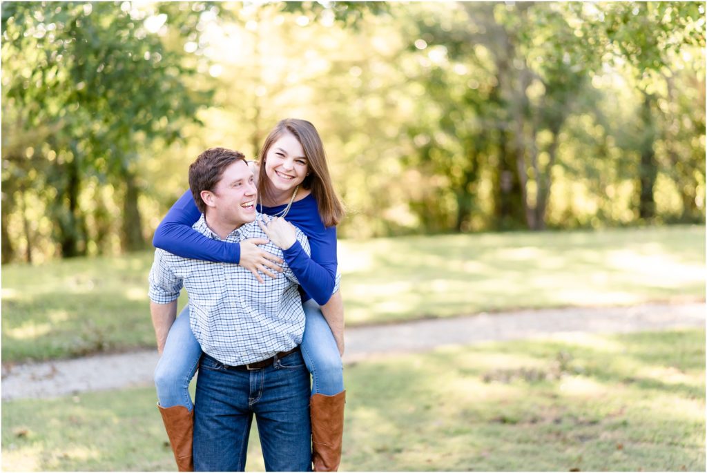 couple smiling and laughing doing a piggyback ride for engagement session at quigg commons in Jefferson City, mo