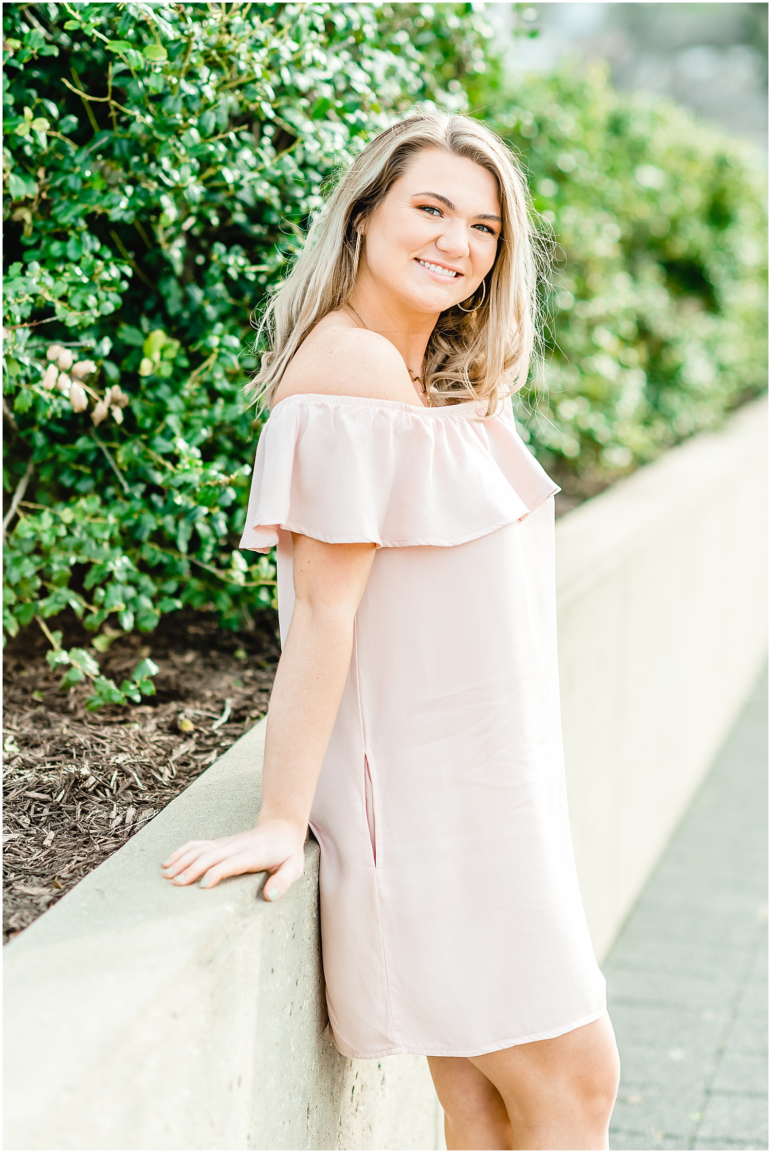 senior girl posing in pink dress for downtown jefferson city high school senior session by green bushes on sidewalk