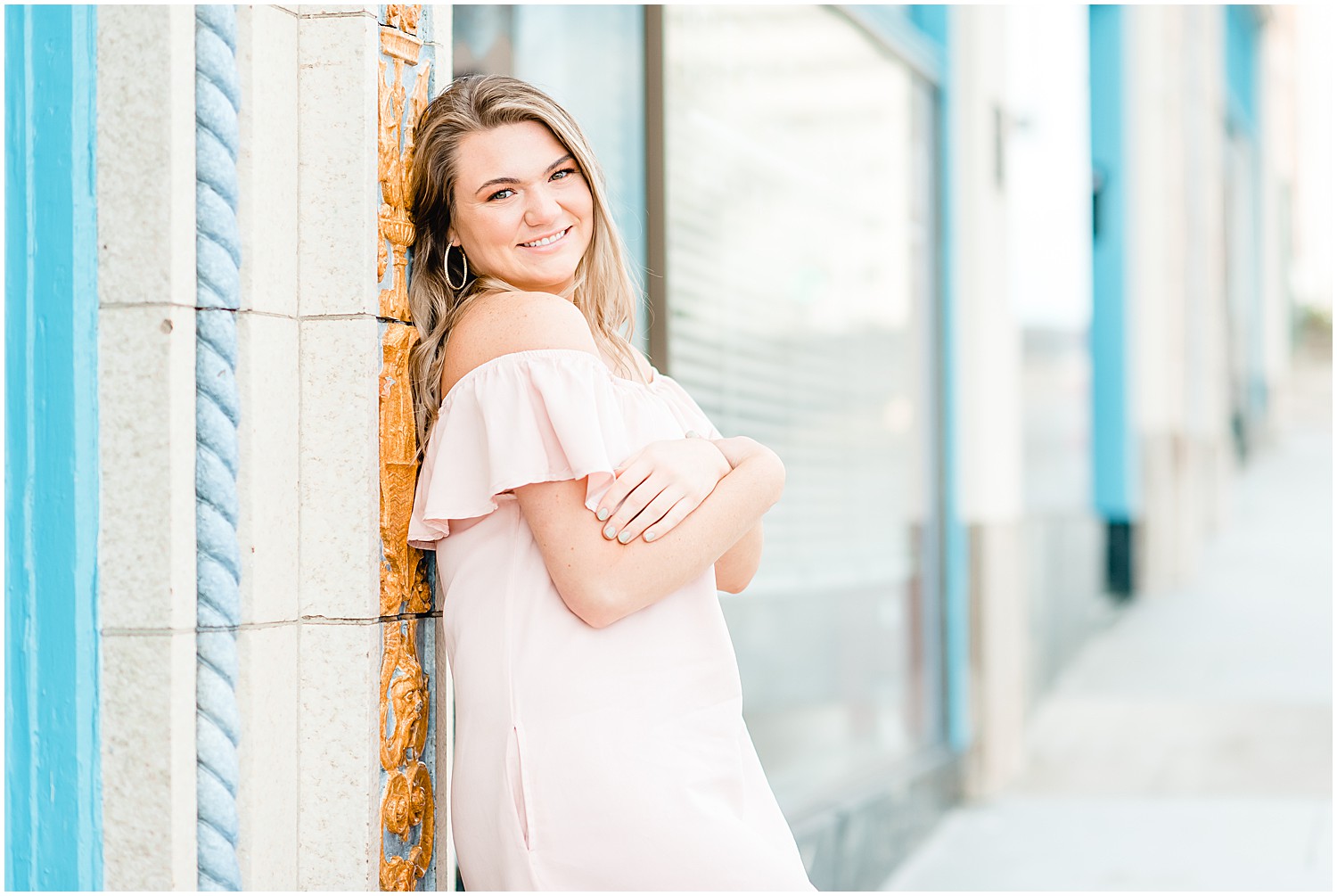 senior girl posing in pink dress for downtown jefferson city high school senior session by blue and white building
