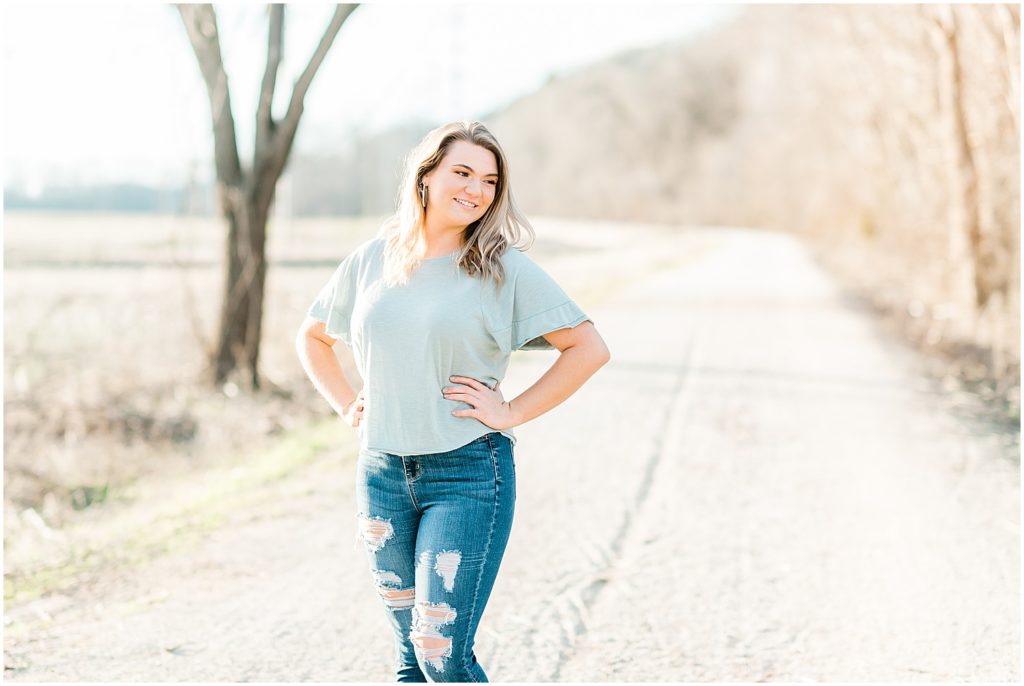 senior girl posing in blue shirt and blue jeans walking on katy trail in the sunlight
