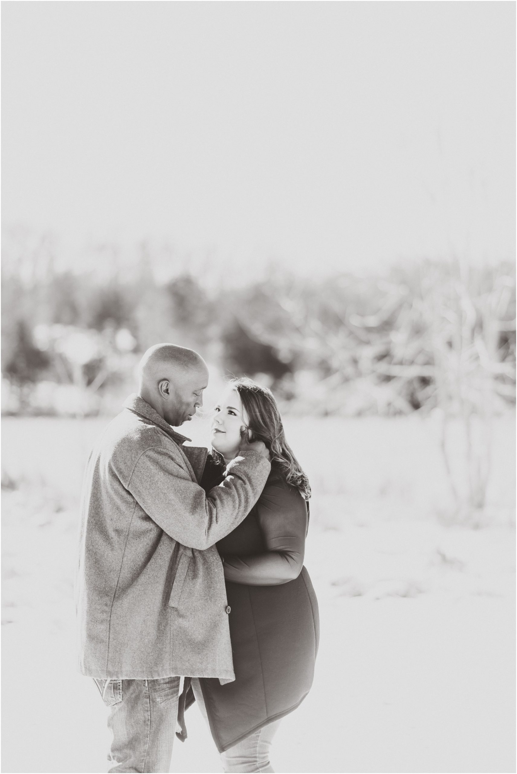 black and white image of engaged couple looking at each other in the snow