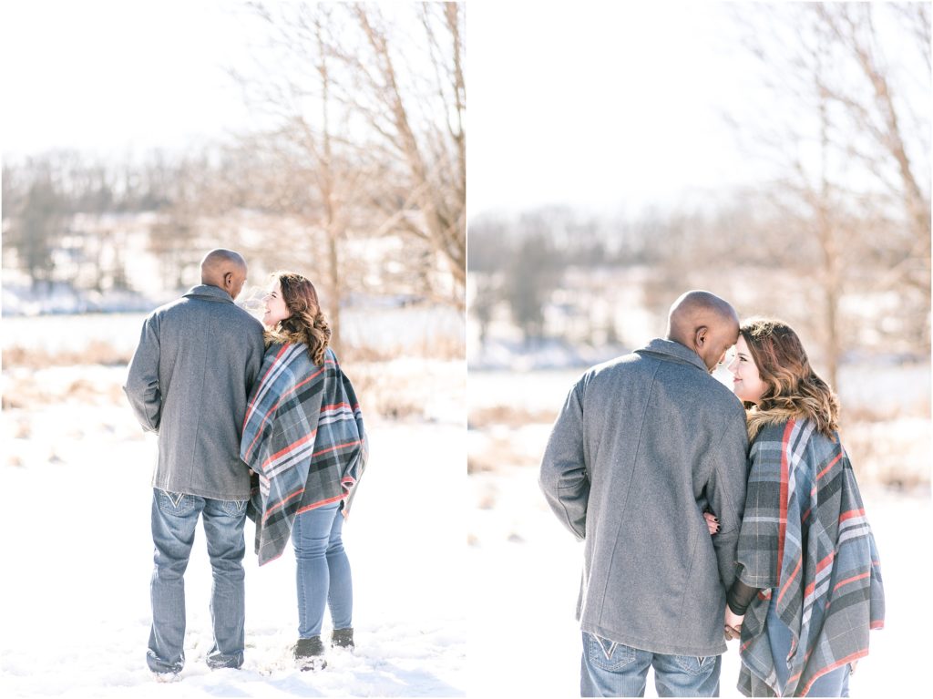 photos of engaged couple turned away from camera smiling at each other wearing a plaid cape in the snow