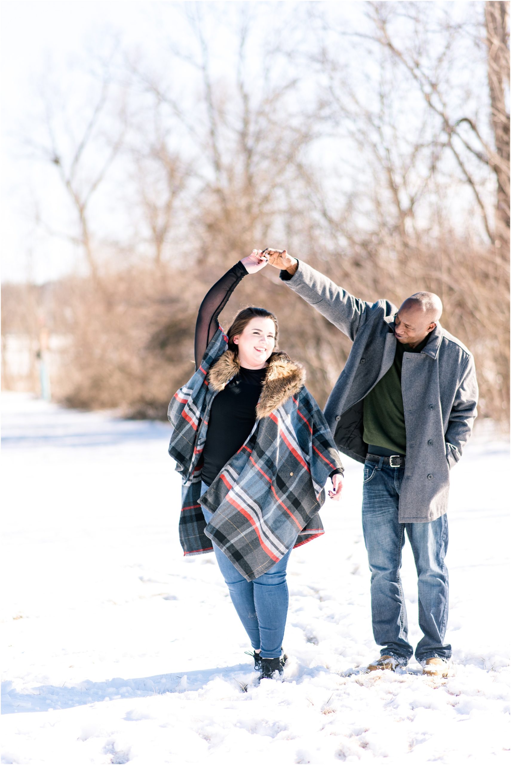 engaged couple dancing in the snow with plaid cape for engagement session