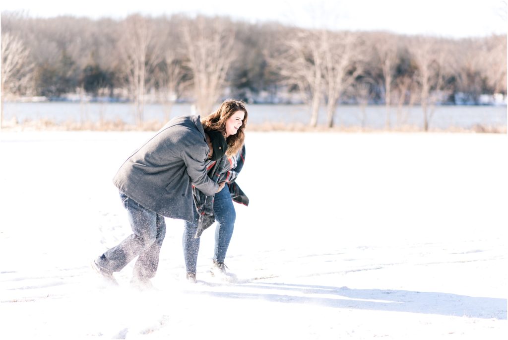 engaged couple wrestling and playing in the snow for engagement session at binder park