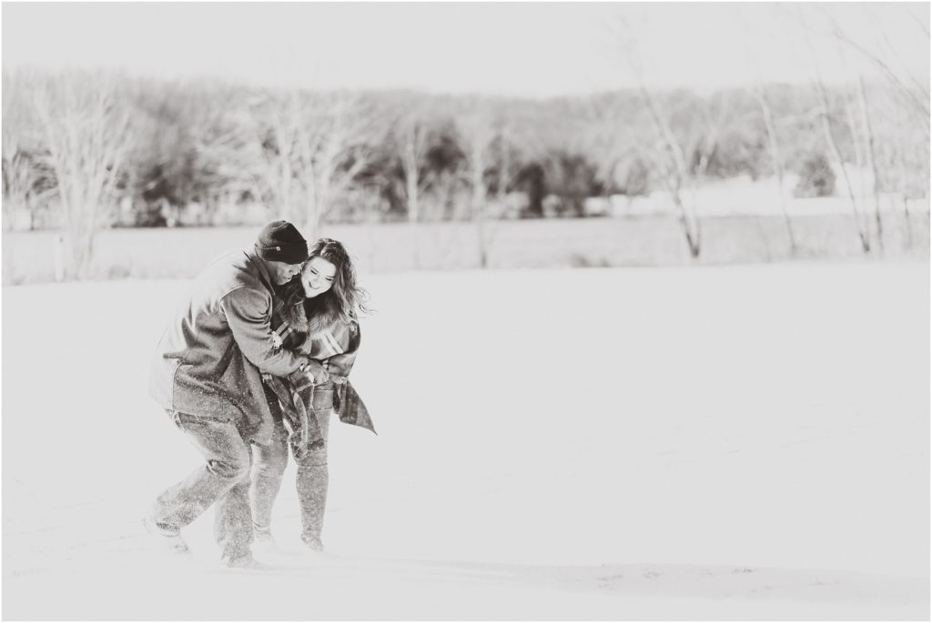 black and white image of mixed race couple playing and wrestling in the snow for engagement session