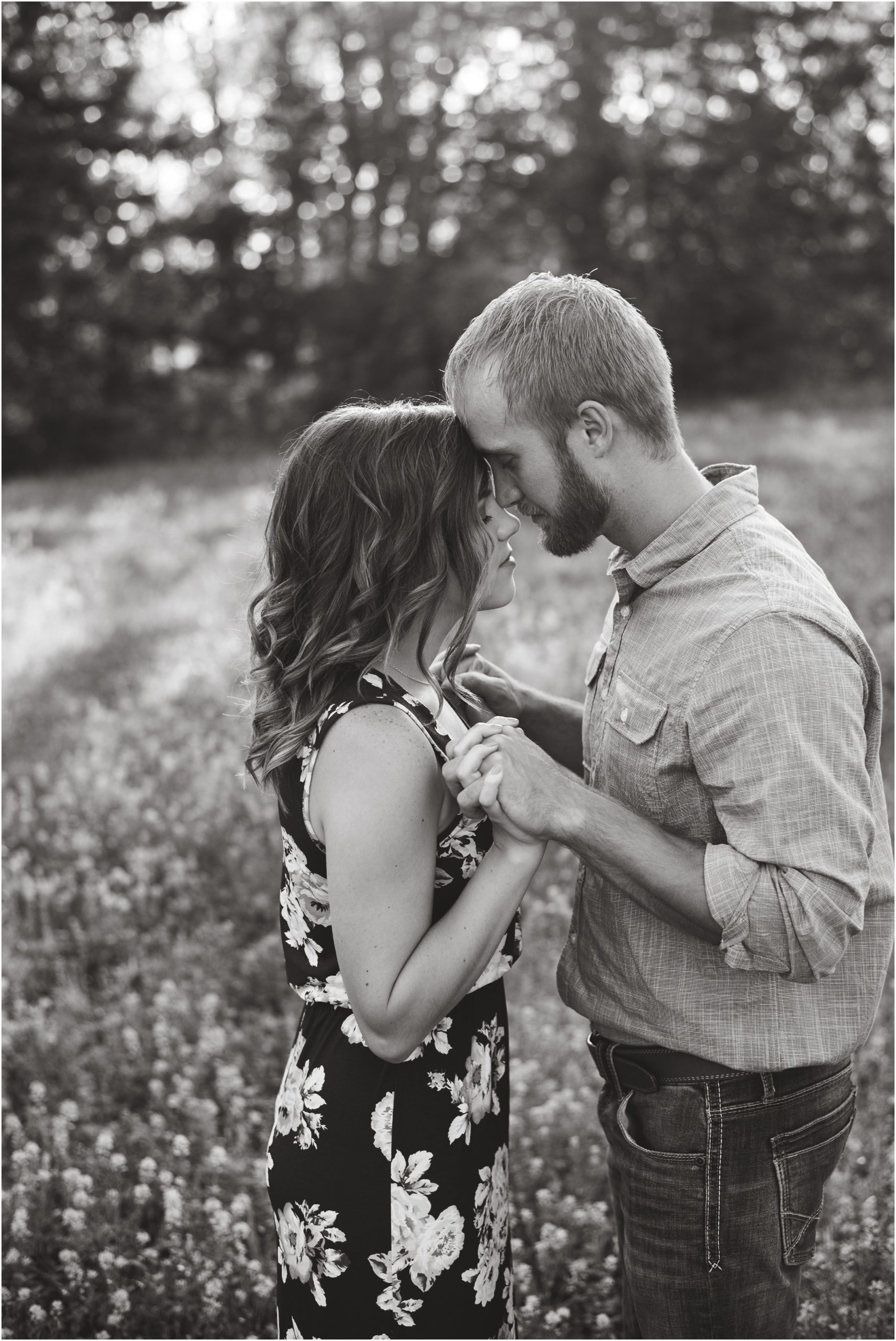 black and white image of couple holding hands and touching foreheads in field for portraits