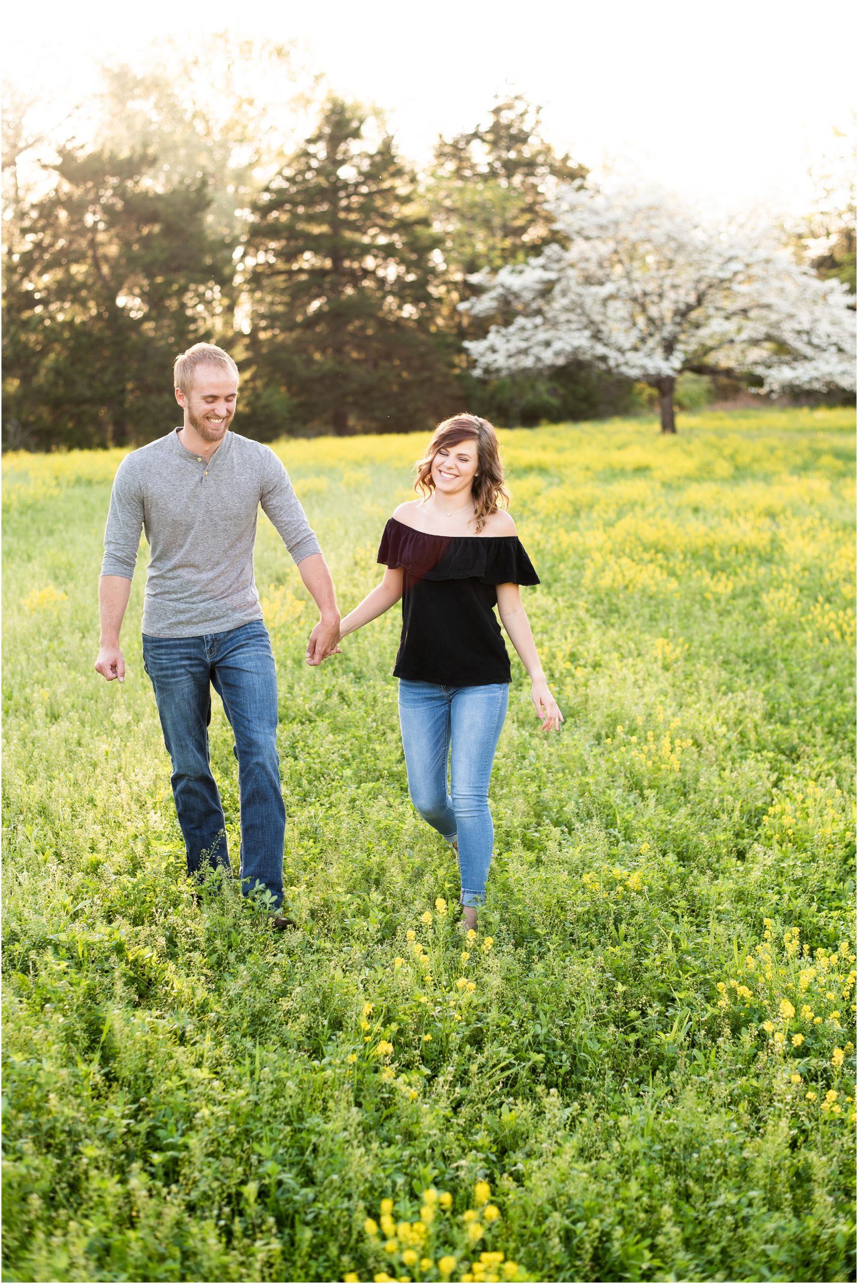 couple laughing walking through wildflower field with white tree in background for couples photos