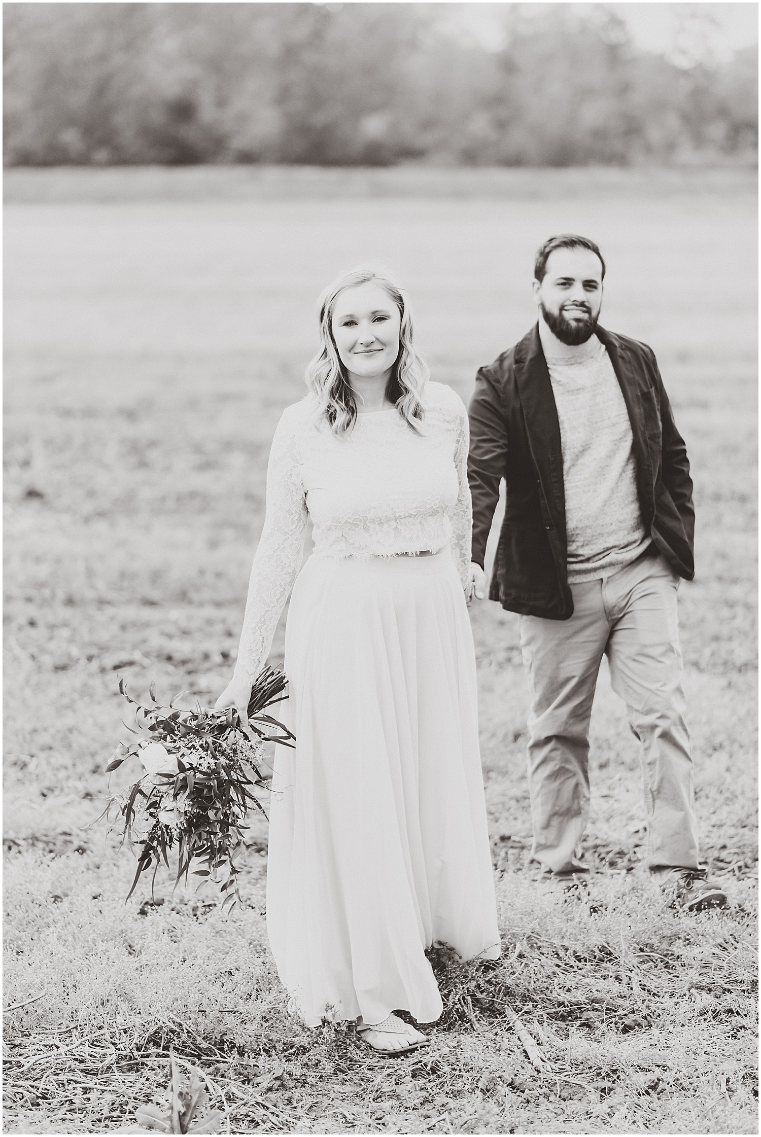 black and white image of couple walking next to each other in field holding bouquet