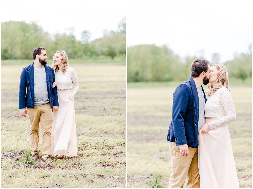 husband and wife in navy and pink walking and kissing in field for portraits