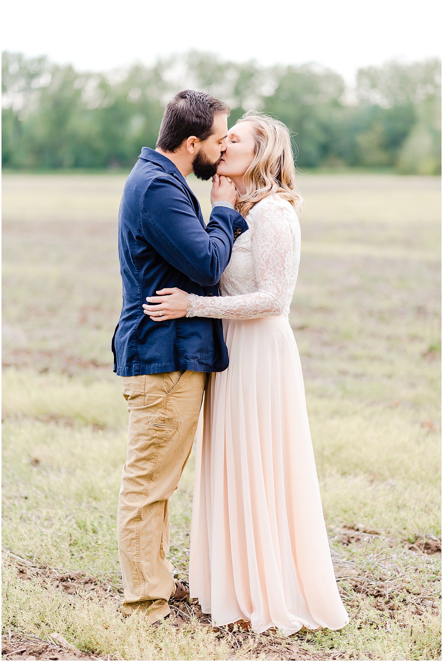 husband in blue blazer and wife in pink skirt kissing in a large field during anniversary session