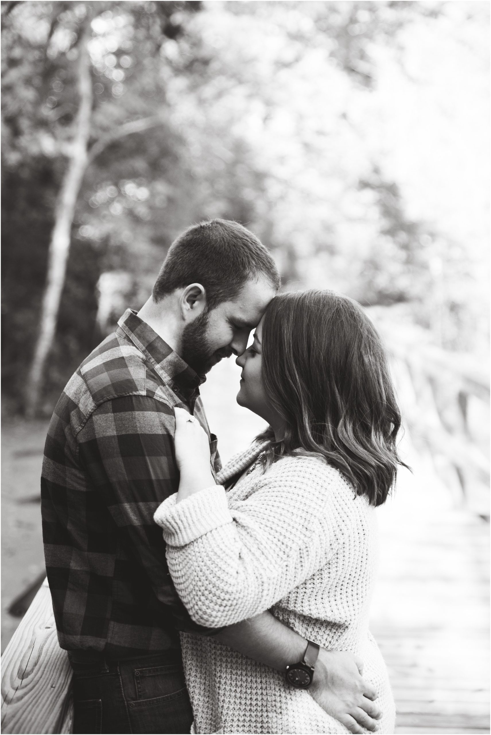 black and white image of couple touching foreheads for engagement session on bridge