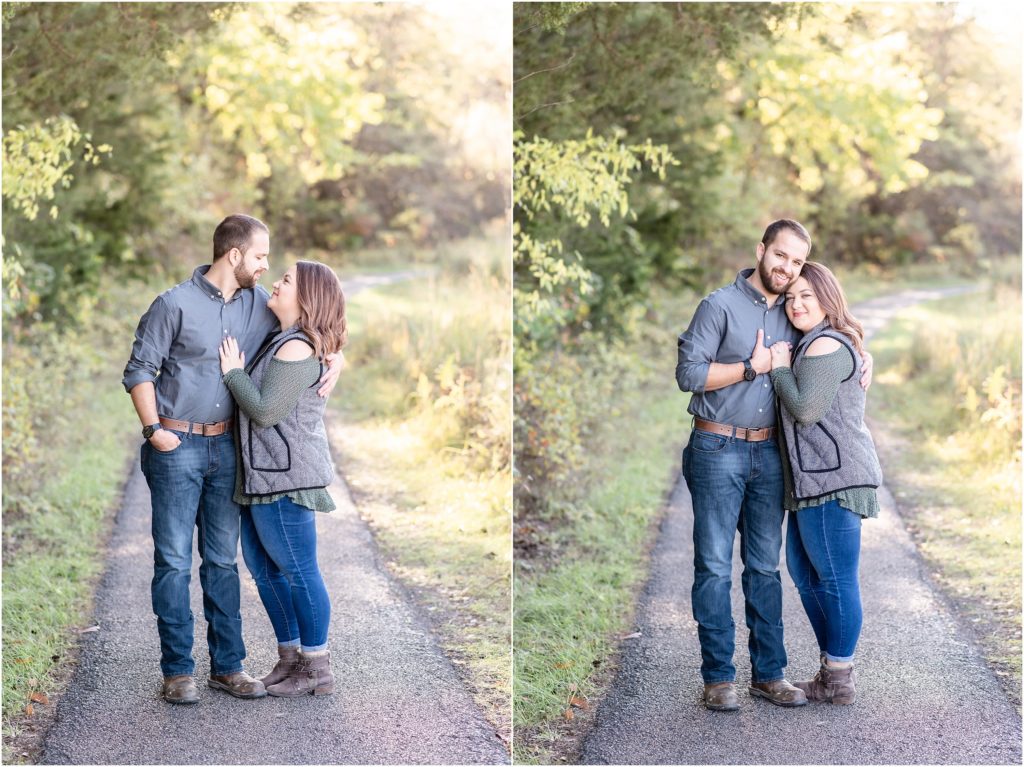 engaged couple standing on path under trees in jeans and vest for engagement session at runge nature center