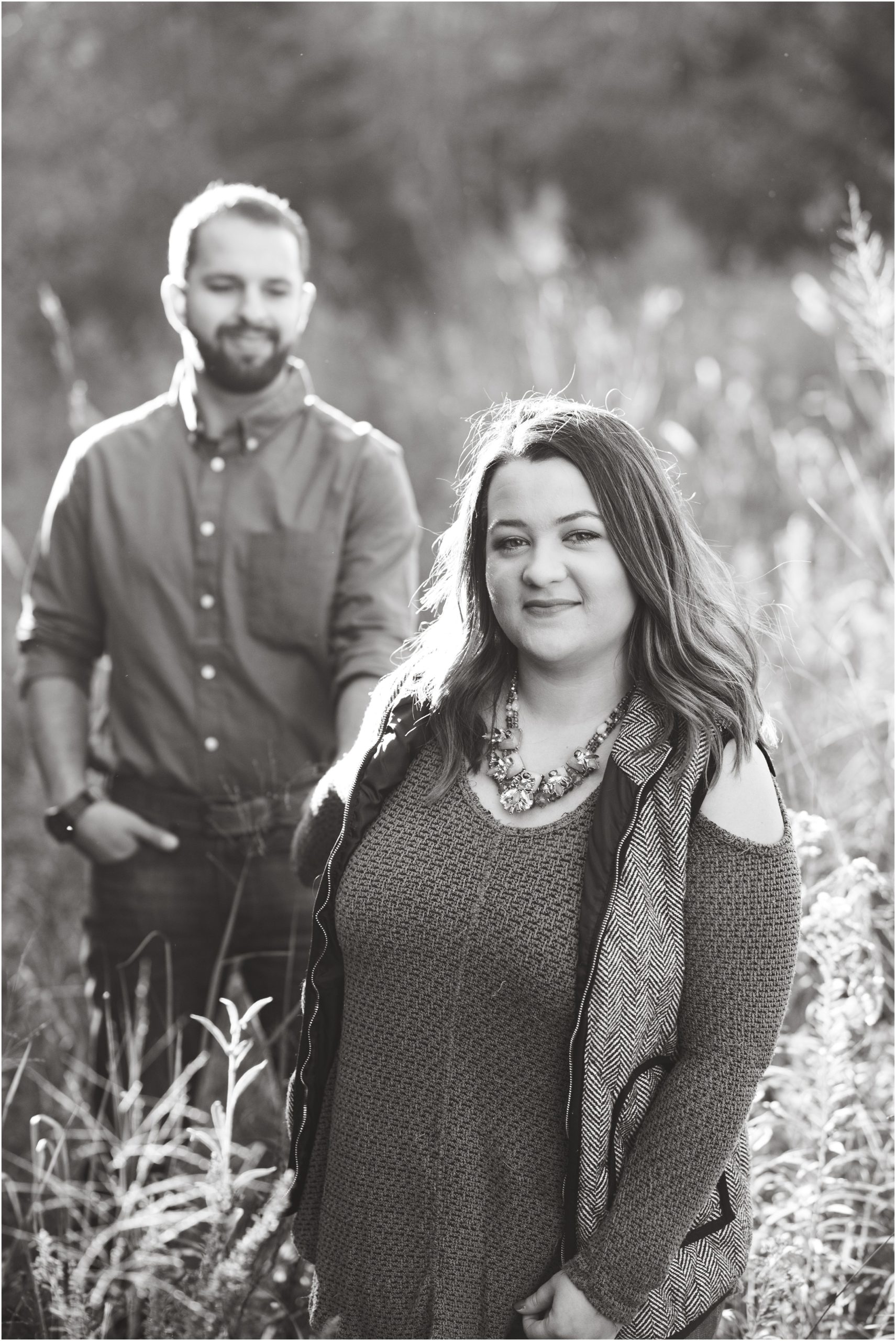 black and white image of engaged couple walking in tall grass for fall engagement session