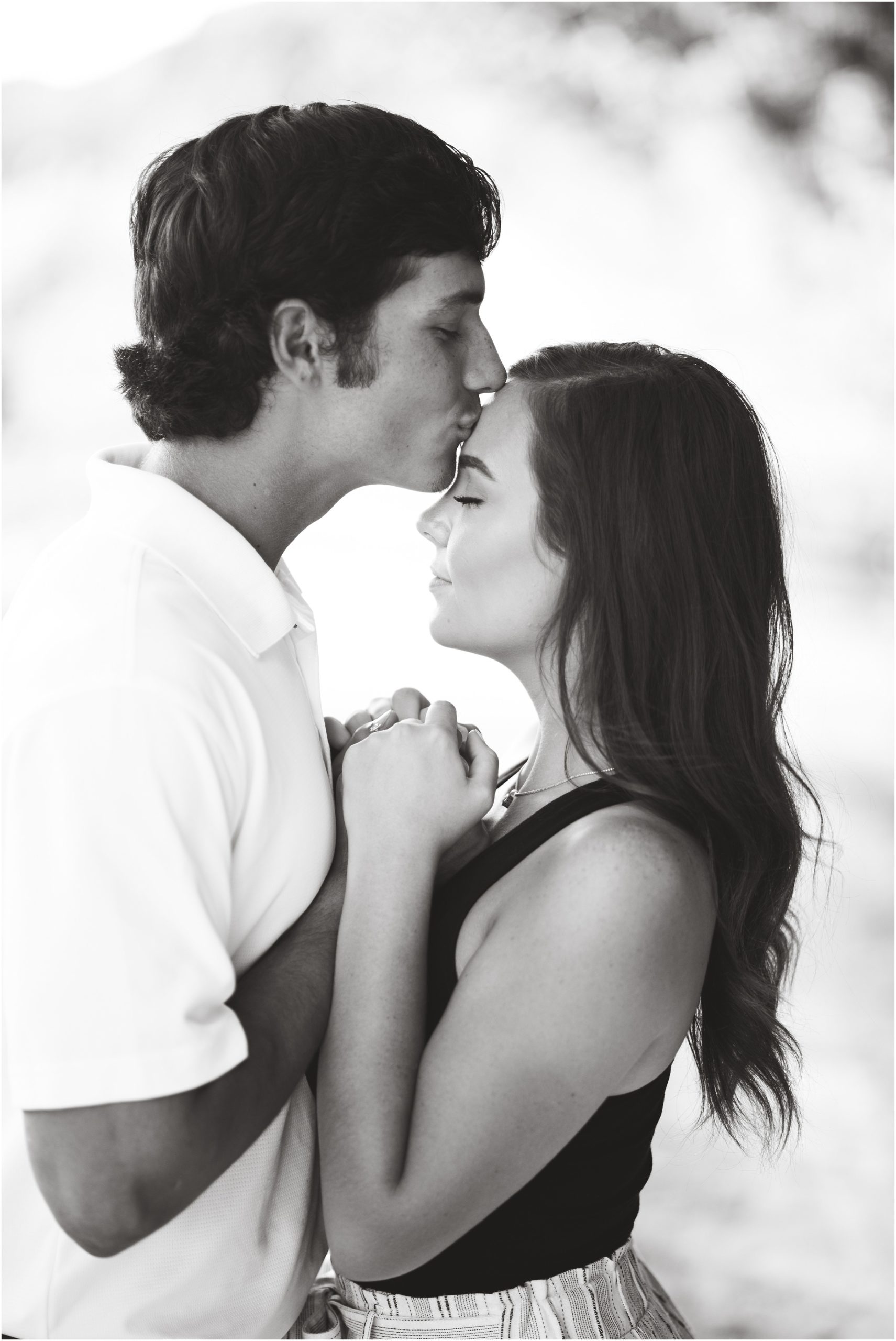 black and white image of boy kissing fiancé on forehead during engagement session