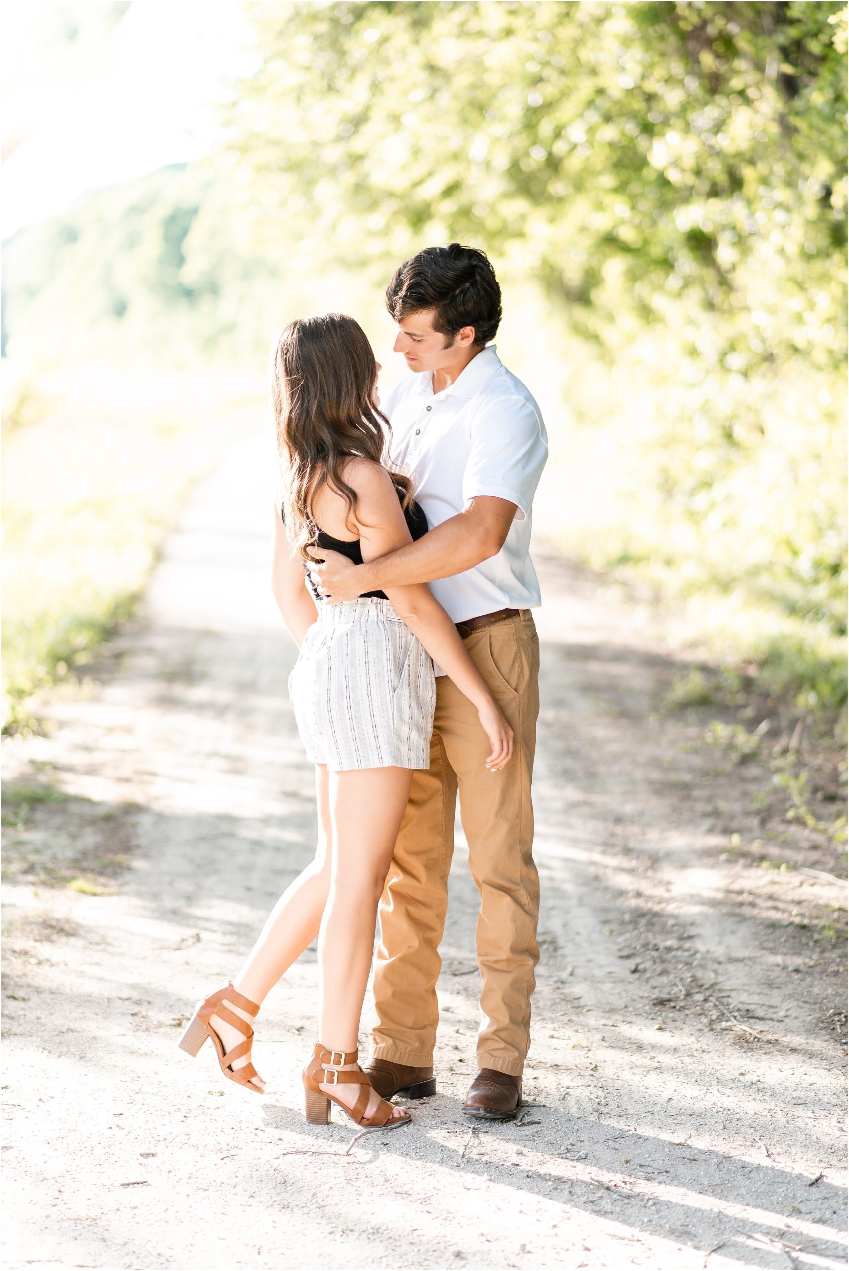 couple embracing in sunlight on gravel path during engagement session