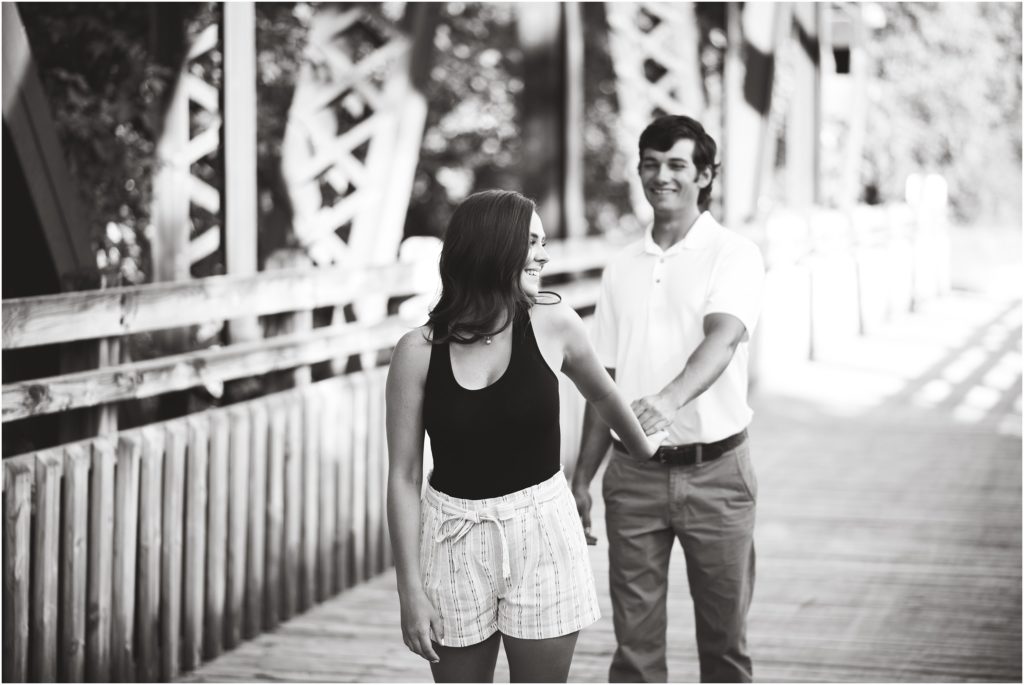 black and white image of girl pulling along fiancé on bridge