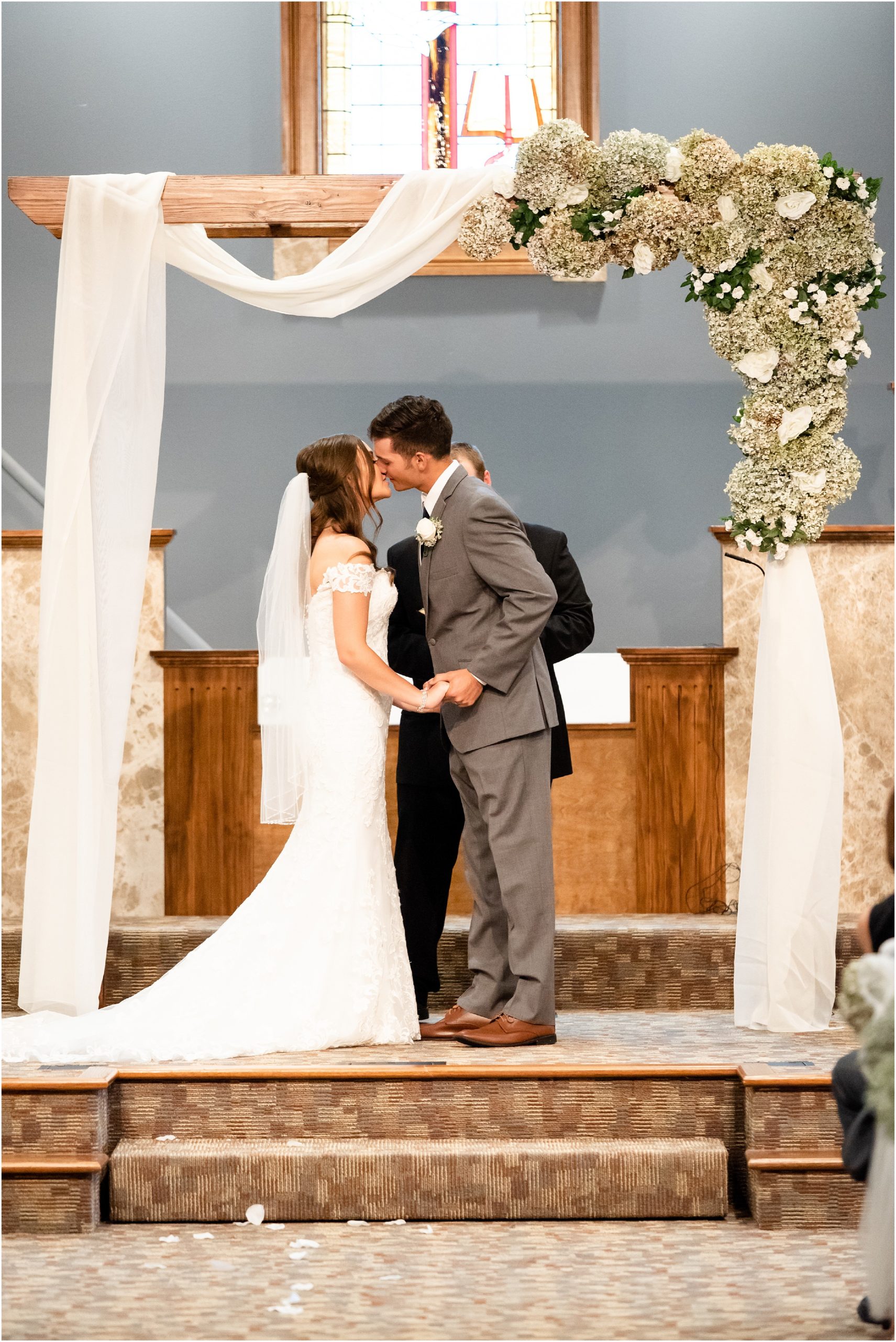 bride and groom first kiss under floral and white curtain arch