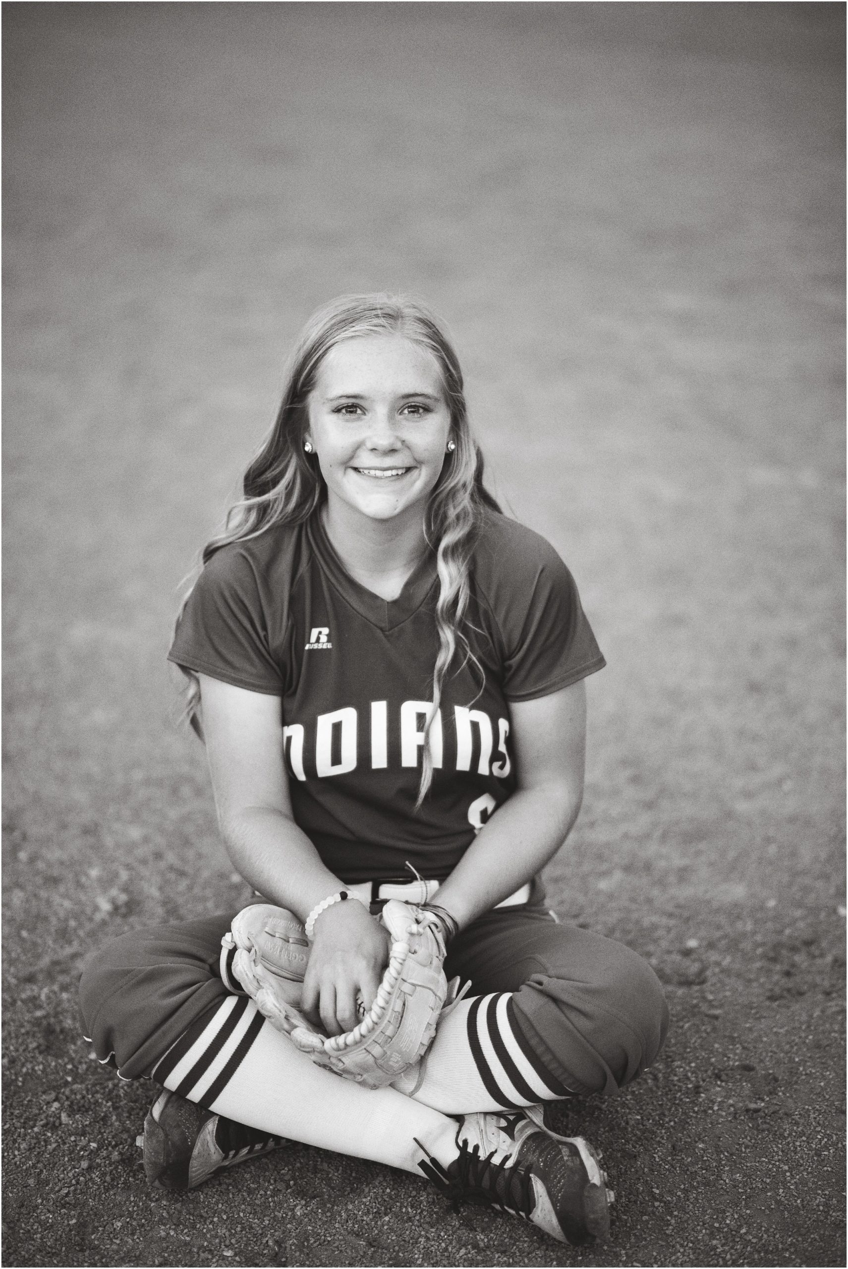 black and white image of senior girl posing for senior session in Russellville Indians softball uniform on softball field