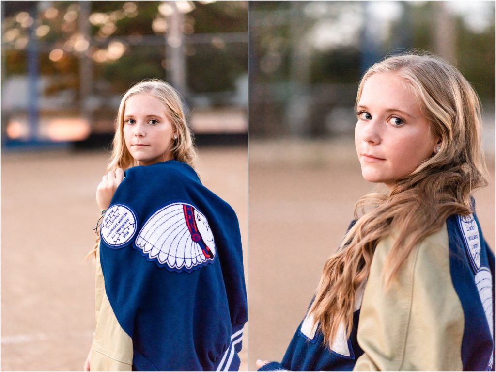 senior girl posing with letter jacket for softball on softball field for senior photos