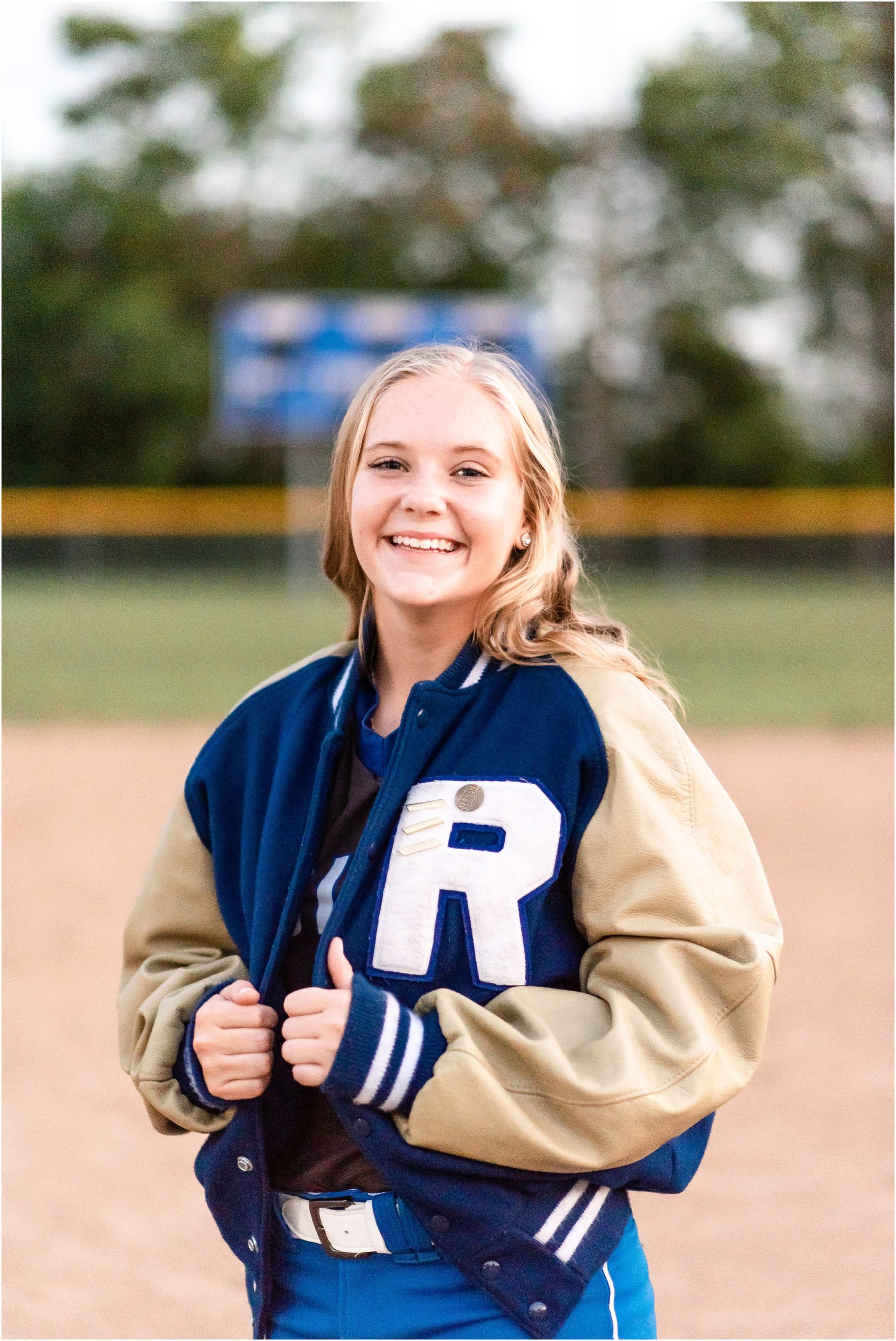 senior girl smiling in letter jacket for Russellville high school senior session on softball field