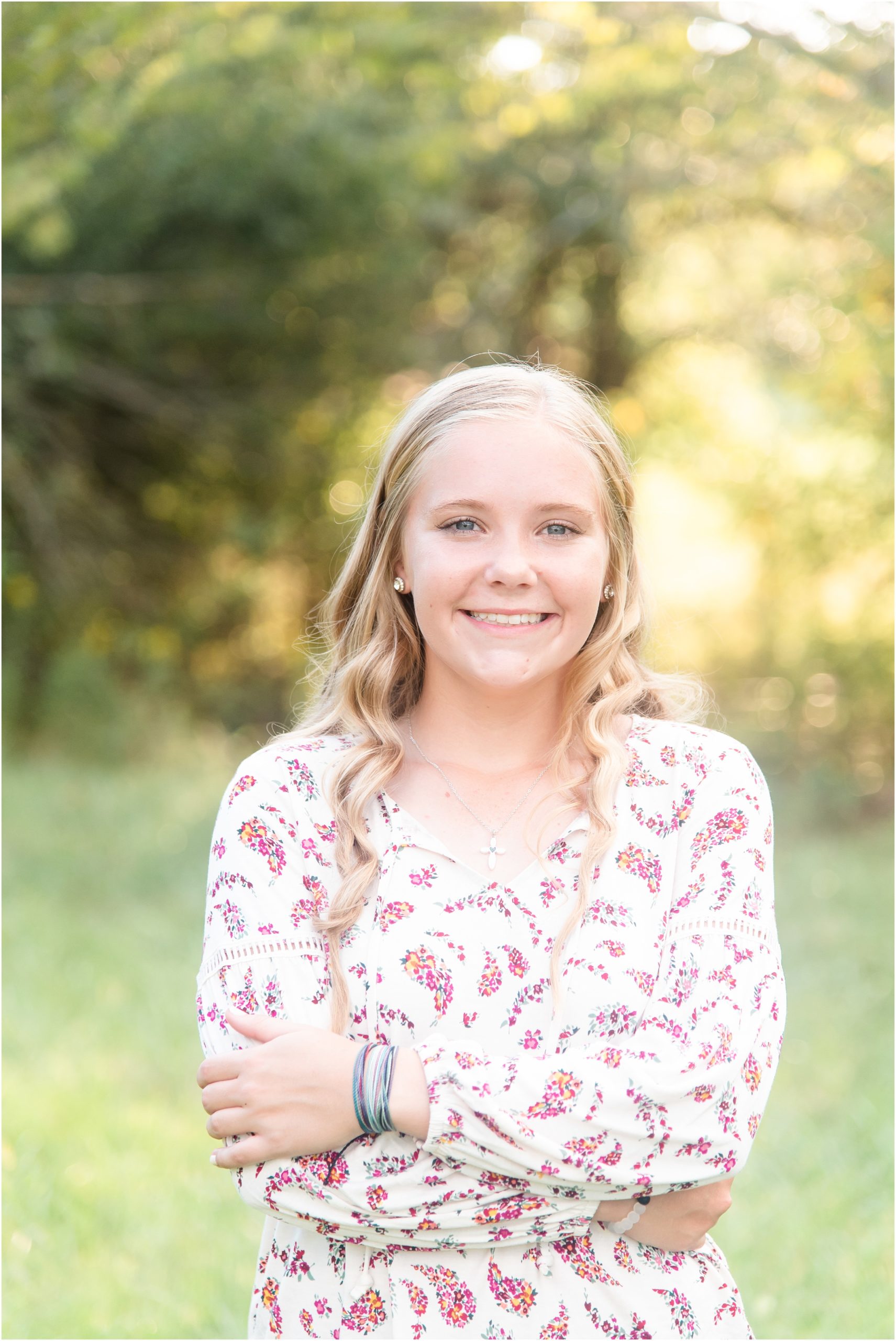 senior girl in floral shirt smiling at camera for senior session in sunlight on family farm in Russellville, mo